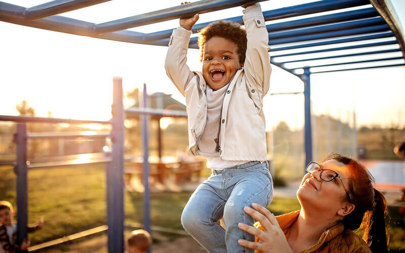 Mother holding child up to swing on playground